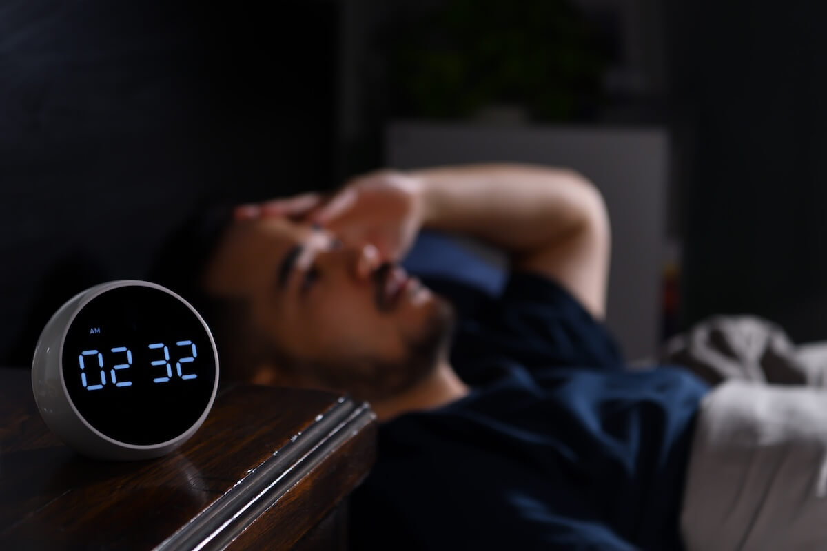 Shutterstock: Depressed young Asian man lying in bed cannot sleep from insomnia. focus on clock