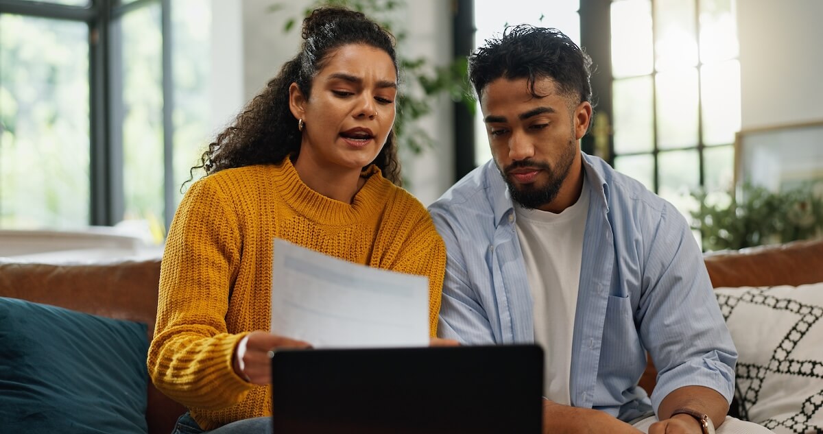 Shutterstock: Home, talking and couple with bills in lounge, financial plan and asset management with information. Serious, man or woman with paperwork for analysis, laptop or discussion with report in living room