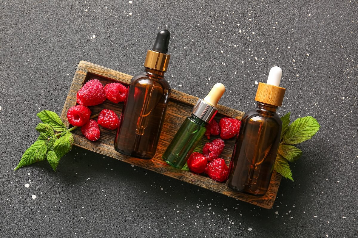 Shutterstock: Wooden tray with bottles of cosmetic raspberry oil on black background