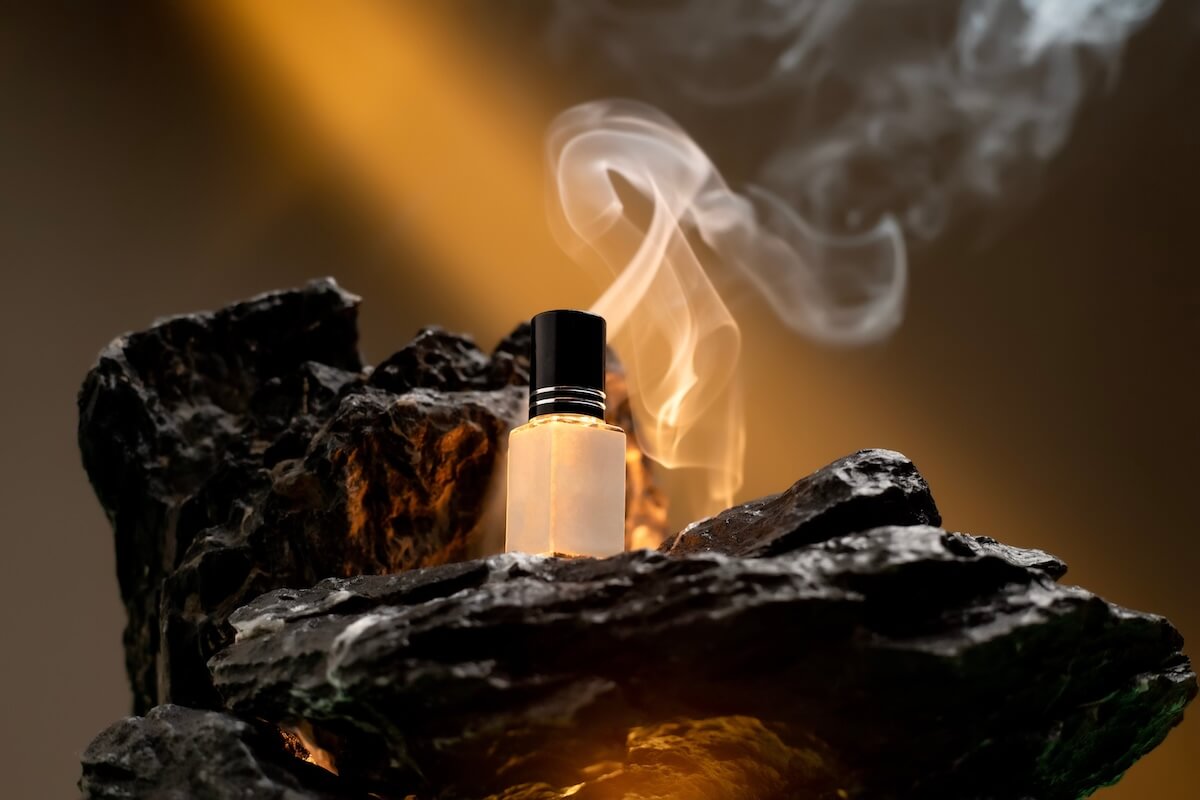 Shutterstock: The image showcases a luxurious perfume bottle on black rocks, adorned with warm lighting and white smoke. The background transitions from warm to darker shades, enhancing the product's appeal.