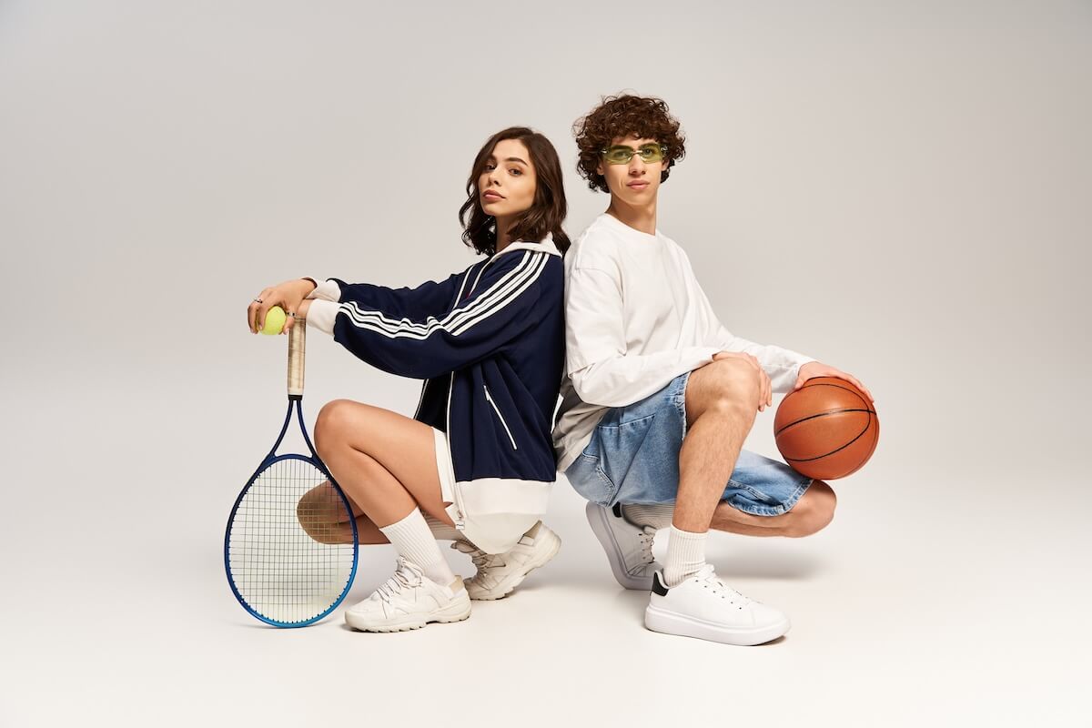 Shutterstock: Trendy couple poses back to back with sports gear, showcasing their love for fun.