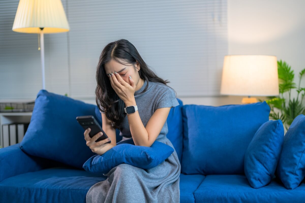 Shutterstock: Stressed Asiaa woman is crying while using smartphone and sitting on sofa at home