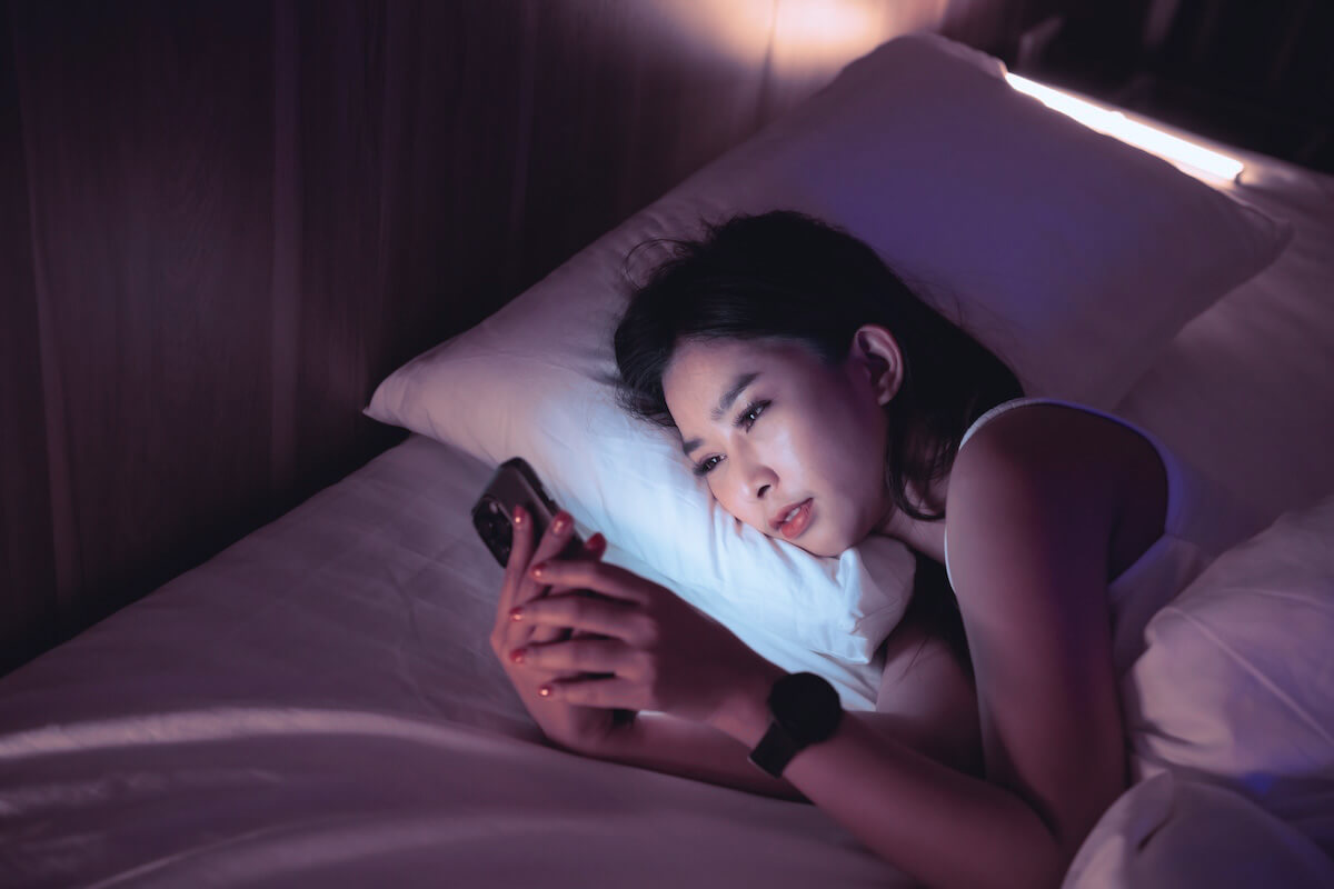 Shutterstock: Woman looking at phone in bed