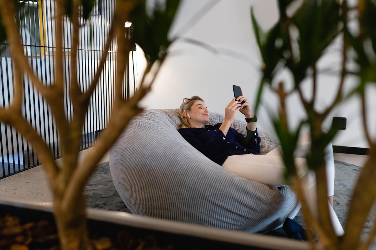 Shutterstock: Side view of a Caucasian businesswoman wearing smart clothes and earphones, working in a modern office, sitting on a bean bag and using a smartphone, Social distancing