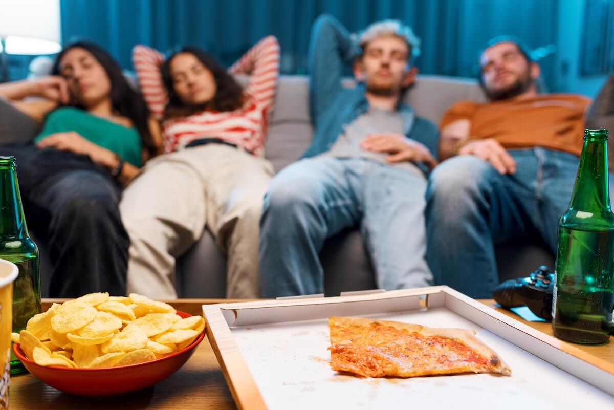 Shutterstock: Lazy friends napping on the couch after eating pizza together