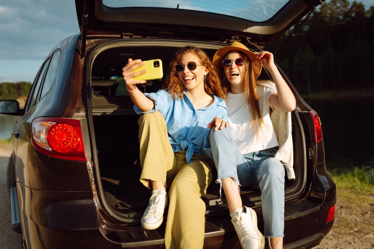 Shutterstock: Friends taking selfie in the back of a car on a road trip