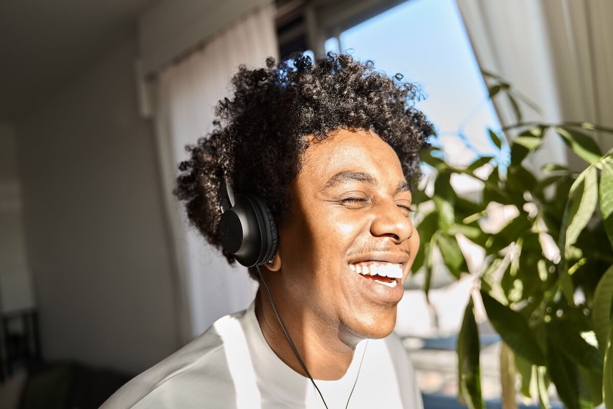 Shutterstock: Happy funky gen z hipster African American guy wearing headphones laughing at home, listening music, having fun feeling relaxed standing in living room at home. Close up authentic shot.