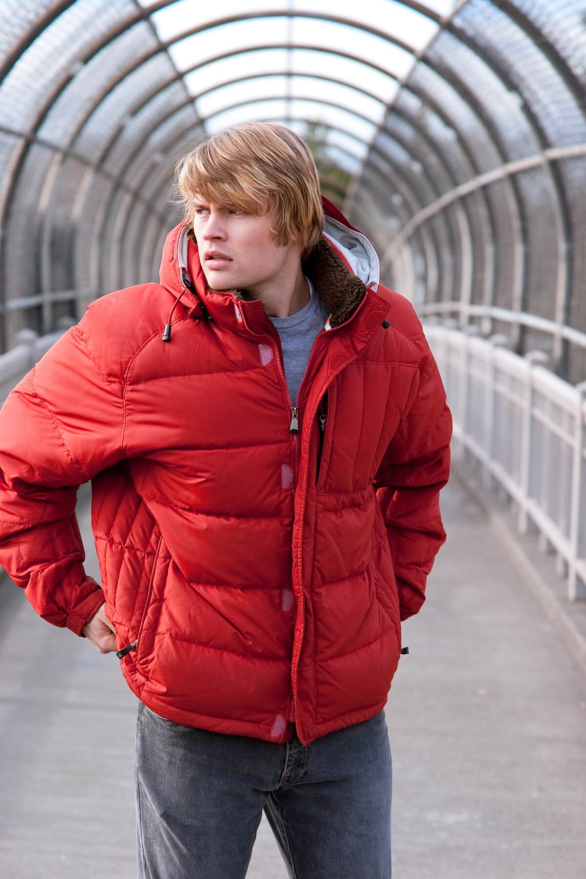 Shutterstock: A male model with his hands at his sides on a covered walking bridge wearing a bright red jacket.