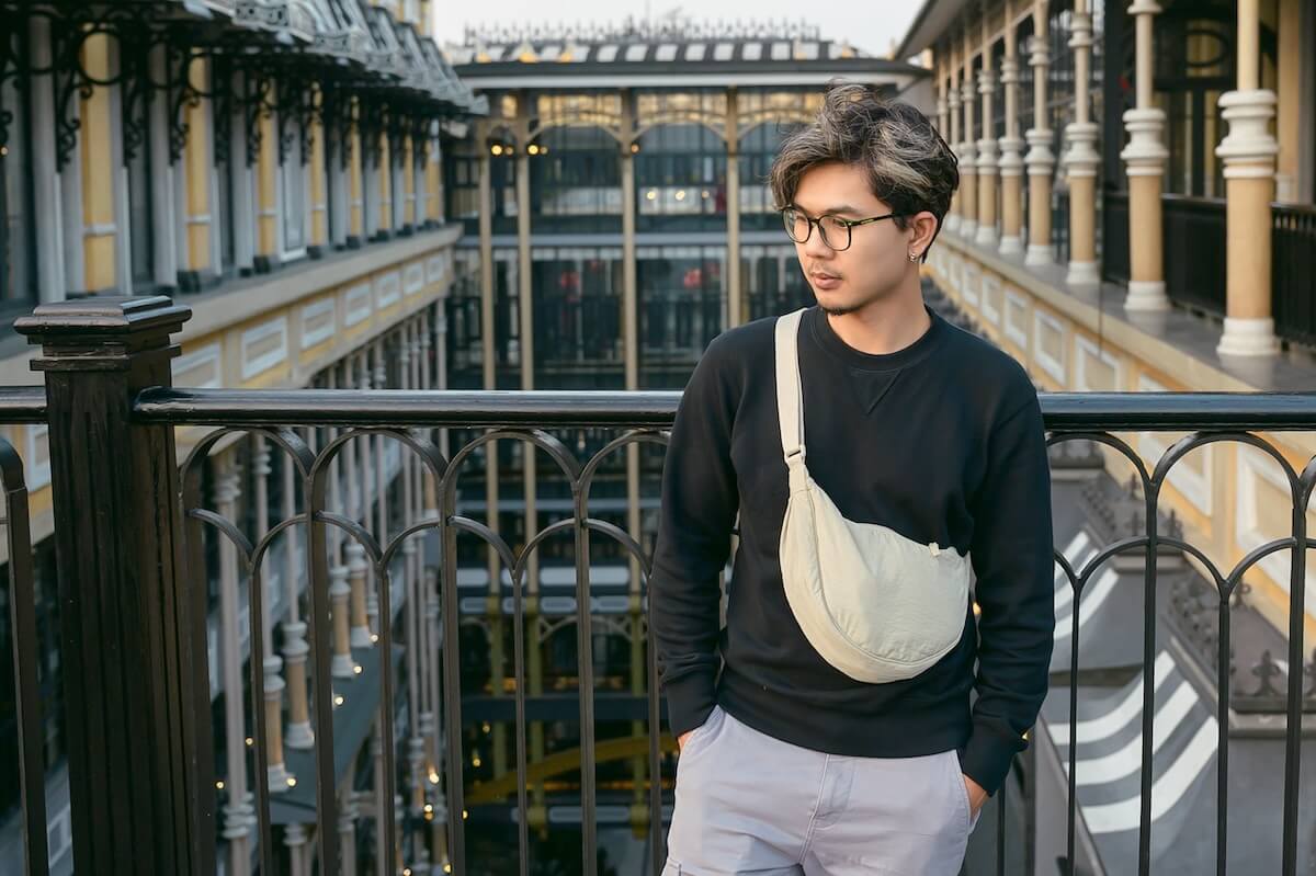 Shutterstock: Stylish Asian man standing on a balcony inside a modern shopping arcade in Hanoi, Vietnam, wearing a black sweatshirt and crossbody bag during his travels.