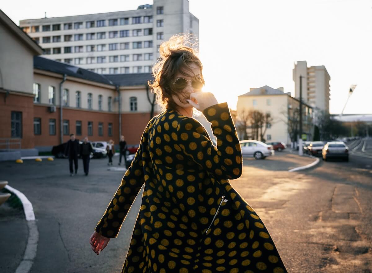 Shutterstock: Attractive young woman with wind disheveled hair wearing polka dot coat and fashion sunglasses turns around at camera on street at sunset.