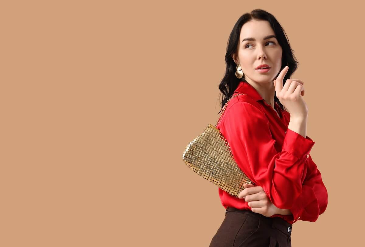 Shutterstock: Beautiful young woman with stylish golden bag on beige background with space for text